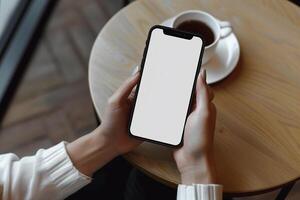 handen Holding telefoon met wit mockup scherm tegen koffie tafel backdrop foto