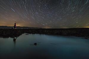 ai gegenereerd een persoon staand Aan rotsen Bij nacht met ster trails foto