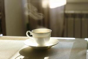 kop van heet stomen koffie Aan een zonnig ochtend- Aan de keuken tafel foto