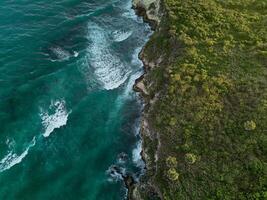 antenne. donker turkoois water met wit schuimend golven en groen rotsachtig kust foto