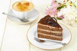 stukje chocoladetaart, cappuccino, bloemen op tafel foto