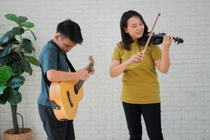 Aziatisch jongen spelen gitaar en moeder spelen viool, voelen gewaardeerd en aangemoedigd. concept van een gelukkig familie, aan het leren en pret levensstijl, liefde familie banden foto