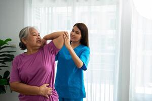 een jong Aziatisch Dames fysiotherapeut verpleging is assisteren een ouderen vrouw oefening uitrekken spieren Bij huis of een premie kliniek voor herstel, concept van fysiek therapie. foto