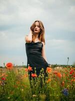 mooi jong meisje in een zwart avond jurk poseren tegen een papaver veld- Aan een bewolkt zomer dag. portret van een vrouw model- buitenshuis. regenachtig het weer. grijs wolken. foto