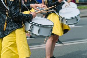 detailopname van handen van vrouw drummers in geel zwart wijnoogst uniform Bij optocht. straat prestatie. optocht van majorettes foto