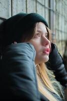 portret van een mooi tiener- meisje in een zwart winter jasje en hoed tegen de achtergrond van een onvoltooid, vernietigd en verlaten gebouw muur. stedelijk concept. detailopname. foto