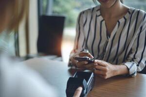 een vrouw betalen Bill door online bank toepassing Aan haar smartphone Bij boodschappen doen winkelcentrum. foto