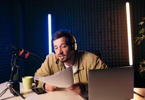 glimlachen en gebaren radio gastheer met hoofdtelefoons lezing nieuws van papier in studio microfoon Bij radio station met neon lichten foto