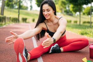 een glimlachen vrouw in sportkleding is opwarming omhoog en uitrekken voordat opleiding in de park. gezond levensstijl concept foto