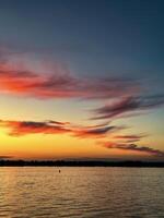 adembenemend zonsondergang schilderij de lucht met tinten van rood en oranje, weerspiegeld subtiel Aan de water voor een perfect vredig avond sfeer foto