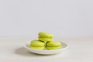 drie licht groen Frans macarons Aan een wit bord en houten tafel. pistache macarons. foto