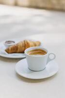 kop van zwart koffie en een croissant Aan een tafel in een straat cafe. foto