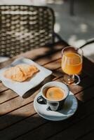 kop van zwart koffie, een croissant en glas van vers oranje sap Aan een tafel in een straat cafe. foto