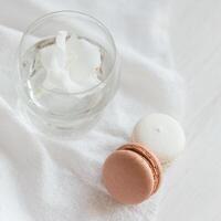 twee pastel Frans macarons en glas met bloem Aan een wit achtergrond. foto