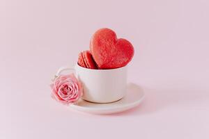 roze hart vormig Frans macarons met roos bloemen Aan een roze pastel achtergrond. concept voor Valentijnsdag dag. foto