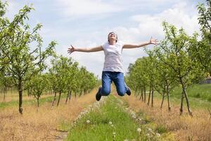 een volwassen vrouw verheugt zich en springt omhoog tegen de backdrop van een bloeiend voorjaar tuin. foto