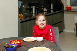 schattig kind meisje Bij huis Bij de tafel in voorkant van een bord van pannekoeken foto