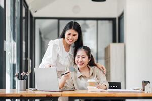 twee vrolijk vrouw collega's genieten een samenwerkend moment in een helder kantoor ruimte, met een richten Bij een laptop scherm. foto