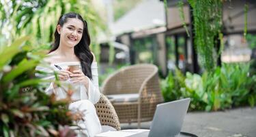 vrolijk freelancer geniet een kop van koffie terwijl werken Aan haar project in de comfort van een tuinachtig buitenshuis werkruimte. foto