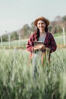 vrolijk vrouw boer staat met een digitaal tablet tussen hoog tarwe gewassen, belichamen modern agrarisch praktijken. foto