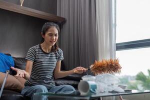 moe jong vrouw Aziatisch in de leven kamer met schoonmaak producten en apparatuur, huishoudster of overweldigd meisje met huiswerk, spanning schoonmaak, huiswerk concept foto