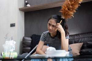 moe jong vrouw Aziatisch in de leven kamer met schoonmaak producten en apparatuur, huishoudster of overweldigd meisje met huiswerk, spanning schoonmaak, huiswerk concept foto