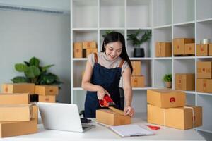 vrouw Aziatisch gebruik Scotch plakband naar vastmaken pakket dozen naar bereiden goederen voor de werkwijze van verpakking, Verzenden, online uitverkoop internet afzet ecommerce concept opstarten bedrijf idee foto