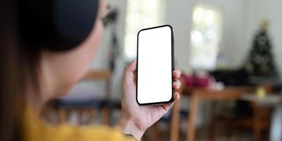 mockup smartphone van een vrouw Holding mobiel telefoon met blanco wit scherm terwijl zittend luister naar muziek- Bij huis foto