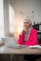 moslim bedrijf vrouw hijab werken over financieel met bedrijf verslag doen van en rekenmachine Aan laptop in huis kantoor foto