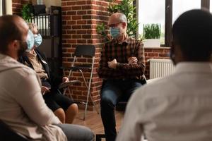 senior man met gezichtsmasker in gesprek met mensen in cirkel tijdens een vergadering foto