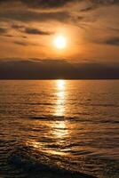 zonsondergang, verlichte zee. een weinig wolken in de lucht, licht golven rollend op de strand foto