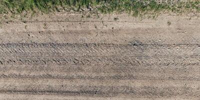 visie van bovenstaand Aan structuur van droog modderig weg met trekker band sporen in platteland foto