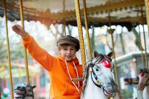 gelukkig jongen ritten Aan een wijnoogst carrousel paard en golven zijn hand. kinderjaren herinneringen. foto