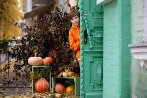 een jongen in oranje kleren looks uit van de deur van een huis versierd met pompoenen voor halloween. foto