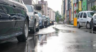 straat in een stad zonder mensen met geparkeerde auto's bij regenachtig weer. regen op de weg. regen en auto's. achtergrond van geparkeerde auto's op een regenachtige stadsstraat. symmetrische geparkeerde auto's. foto
