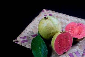 guava geïsoleerd. verzameling van rood vleesgeworden guava fruit met geelachtig groen huid en bladeren geïsoleerd Aan zwart achtergrond met geweven bamboe. foto