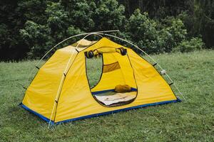 toerist tent voor drie mensen, een plaats naar slaap in natuur, een slapen zak leugens in de tent, metaal boog kader, rust uit in de Woud wandeltocht. foto