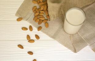 glas van amandel melk met amandel noten Aan canvas kleding stof Aan wit houten tafel. zuivel alternatief melk voor ontgiften, gezond aan het eten en diëten foto