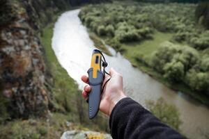 een mooi mes leugens in de palm van een man's hand, een toerist houdt een wandelen mes in een geval, een grijs plastic schede, een reis alleen, zomer vakantie in natuur. foto