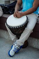 een Afro-Amerikaans Toneelstukken een trommel, de handen van een zwart vent liggen Aan de wit dek van een Afrikaanse djembe trommel, een straat musicus, een een deel van een menselijk lichaam. foto