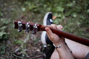 een top visie van de gitaar, een hand- geklemd de frets van de snaren, een man's borstel Holding de toets van de gitaar, een deel van een musical instrument, het zingen liedjes in de bossen. foto