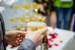 Champagne is gehouden door een man's hand, een vol glas van alcoholisch drank, bubbels van schuim Aan de oppervlakte van de martini. foto