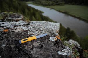 een mes met een plastic geel omgaan met leugens Aan een steen. blad voor snijdend in een wandeltocht, camping uitrusting element. foto