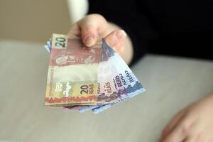 braziliaans geld rekeningen in vrouw hand. vrouw geeft bundel van braziliaans reais naar ons foto