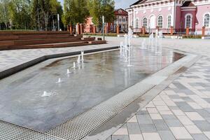 een fontein in de stad- vierkant, stralen van water stijgende lijn van hieronder van onder de stoep, een onderhoudend fontein voor kinderen, dansen spatten van water Aan een zomer dag. foto