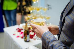 Aan een feestelijk avond, mensen drinken Champagne in bril, een hand- houdt een martini gegoten in een driehoekig glas, een Mens drankjes Bij een partij, een detailopname foto. foto