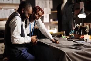 ervaren Afrikaanse Amerikaans atelier winkel collega's minutieus snijdend verfijnd textiel materiaal voor klant in opdracht pak. deskundige pakmakers fabricage op maat gemaakt kleermakers- kleding foto