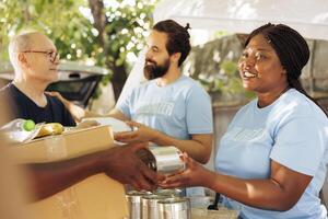 Afrikaanse Amerikaans en Kaukasisch vrijwilligers voorzien hulp, geven bijdrage dozen gevulde met niet bederfelijk items naar de arm. multi-etnisch team helpt strijd honger en armoede door liefdadigheid pogingen. foto
