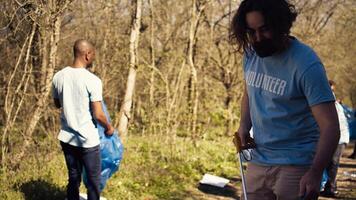 Mens activist gebruik makend van tang naar grijp vuilnis en plastic afval, plukken omhoog uitschot en schoonmaak de Woud Oppervlakte. vrijwilliger sorteren onzin en recycling het, bewaren de natuur. camera b. foto