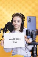 vrouw filmen promotionele voor wereld boek dag gebruik makend van microfoon en telefoon, studio achtergrond. inhoud Schepper bevorderen lezing, winnen bewustzijn voor literatuur belang foto